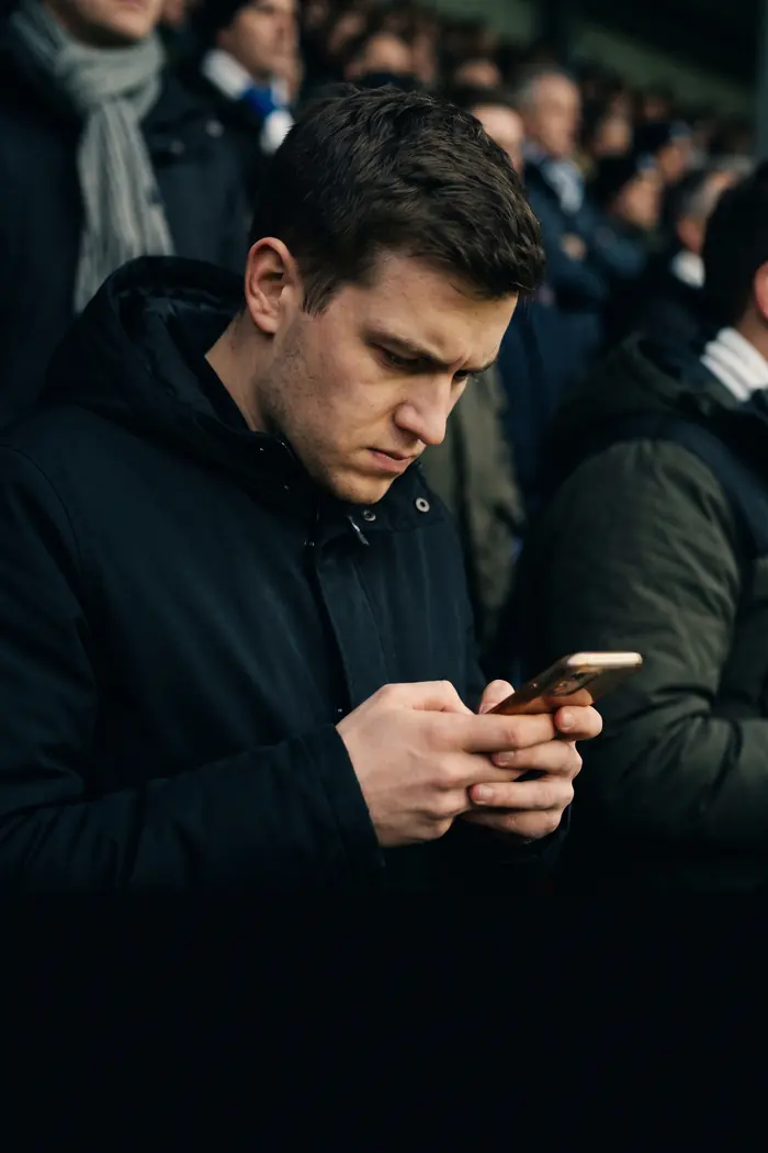 A supporter in the stands at night, lit by his phone screen